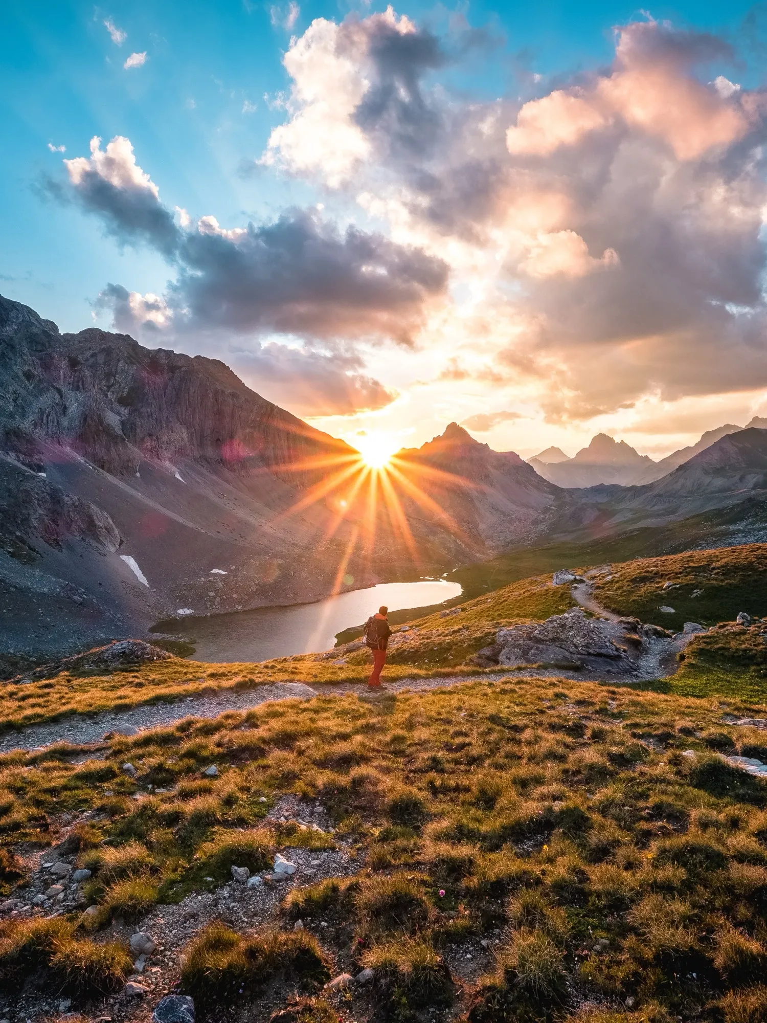 Un randonneur au-dessus d'un lac de montagne, face au soleil couchant