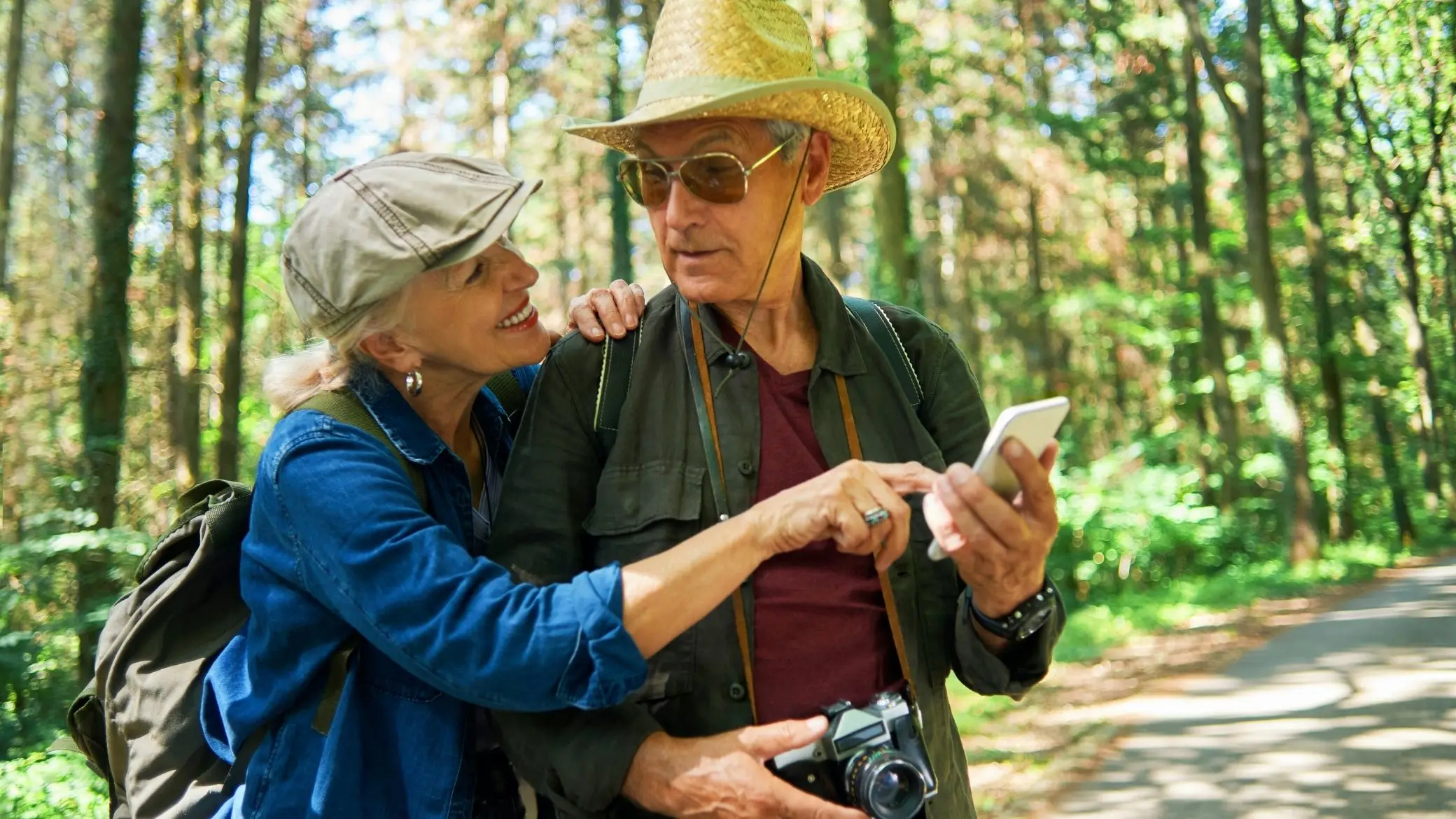 Un couple de randonneurs regarde l’écran d’un téléphone sur un chemin en forêt
